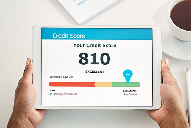 Mercado Pago: mãos segurando um tablet visto de cima, onde mostra a pontuação no Serasa indicando score de 810 pontos. Ao lado, uma xícara de café e, acima, uma planilha.