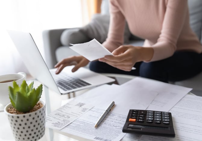 Mulher com computador e calculadora colocando as contas em dia