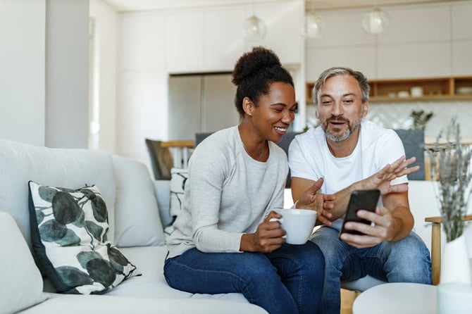 Casal sentado em um sofá olhando o celular e sorrindo