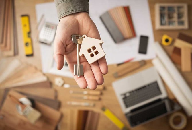 Uma mão segurando um chaveiro com o formato de uma casa e uma chave pendurada. 