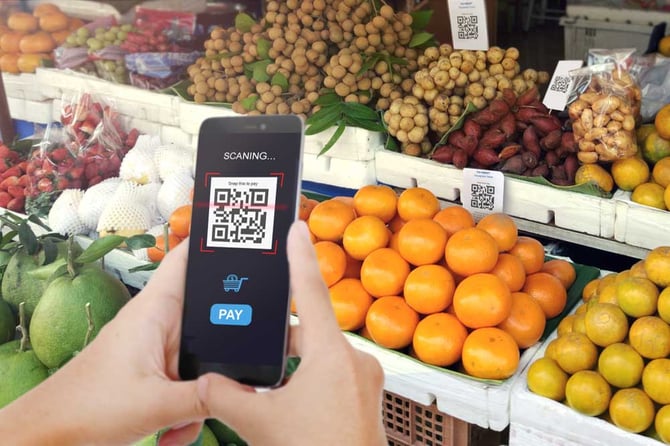 Um celular escaneando um QR Code em uma barraca de frutas para pagar as compras através da Conta Mercado Pago 