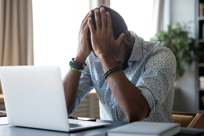 Homem em frente ao computador com as duas mãos na cabeça, olhando para baixo