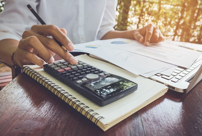 Mercado Pago: pessoa sentada à mesa, fazendo contas em papéis e com uma calculadora, para avaliar se vale mais a pena amortizar ou investir.