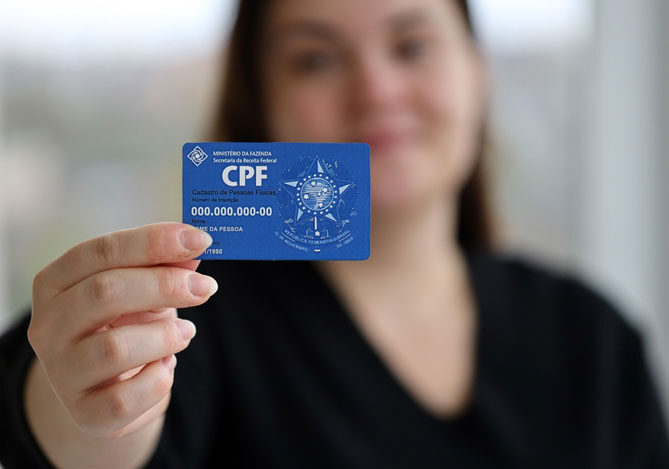 Mercado Pago: imagem de uma mulher vestindo uma camiseta preta e mostrando um documento de CPF, representando a importância de ter atenção com um CPF pendente de regularização e proceder com esse ajuste o mais breve possível.