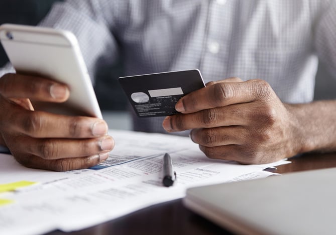 Mãos de uma pessoa segurando o celular e a outra um cartão, sugerindo as movimentações financeiras com o cartão virtual Mercado Pago