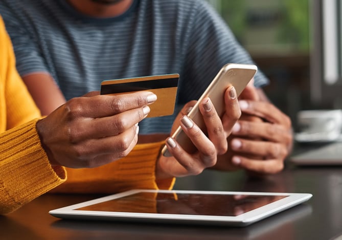 Mulher segurando celular e cartão de crédito enquanto coloca em prática o processo de como comprar criptomoedas com o cartão Mercado Pago