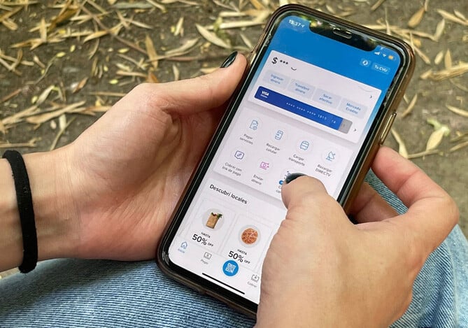 Imagem das mãos de uma pessoa acessando sua conta digital com rendimento automático Mercado Pago via app no celular. Na tela do celular, é possível ver a home do aplicativo da Conta Mercado Pago, com as opções do menu principal.