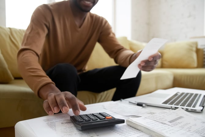 Mercado Pago: homem sentado à mesa, vista de frente, com várias planilhas e calculadora espalhadas para planejar o ano com as contas em dia. 