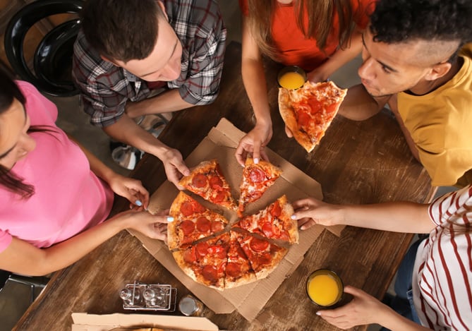 Pessoas em volta da mesa enquanto pegam pedaços de pizza para celebrar o Bitcoin Pizza Day com a compra de criptomoedas no Mercado Pago