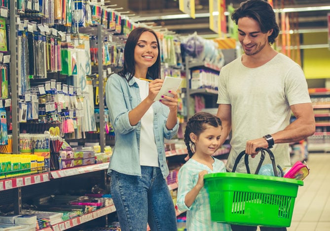 Casal com sua filha em uma loja de material escolar para fazer as compras com economia e auxílio das soluções do Mercado Pago