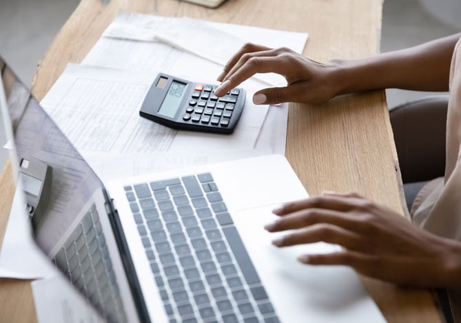 Mãos de uma mulher mexendo no laptop e na calculadora para avaliar as soluções disponíveis do Mercado Crédito, linha de crédito do Mercado Pago