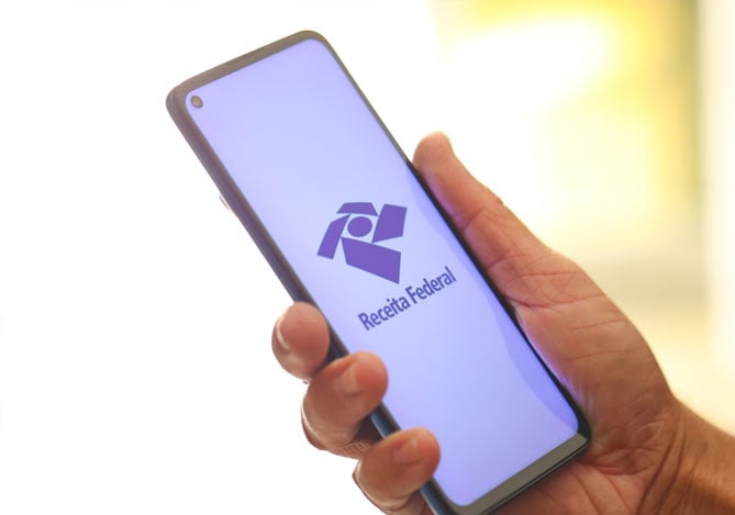 Mercado Pago: mãos de uma pessoa segurando um smartphone que está com a tela ligada e aberta com o logo da Receita Federal aberto