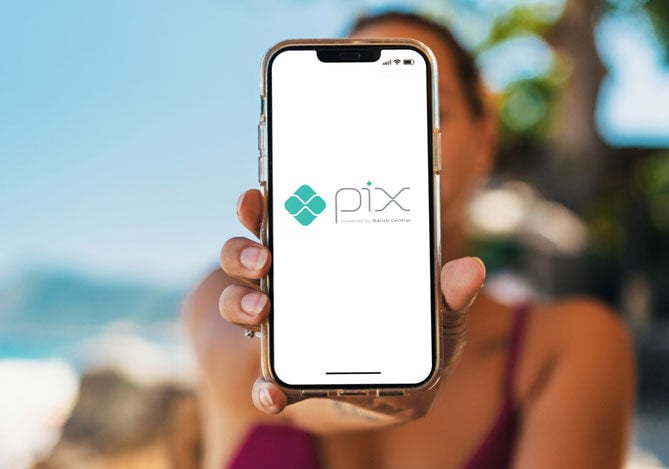 Mercado Pago: Pessoa segurando um celular exibindo o logotipo do Pix, destacando a praticidade e eficiência do pagamento instantâneo durante as férias.