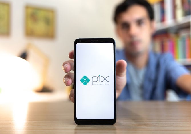 Mercado Pago: Homem segurando e mostrando a tela do seu celular com imagem indicando o Pix Internacional