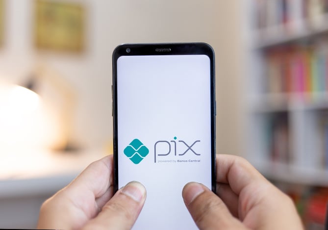 Mãos de uma pessoa mexendo no celular com uma tela ilustrando o logo do Pix no cartão de crédito, que pode ser feito na sua Conta Mercado Pago