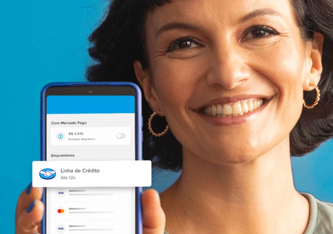 Mulher de cabelo curto, sorridente, usando brincos de argolas pequeno, segurando um smartphone com as mãos e unhas azuis, que mostram a Conta Mercado Pago como a opção que mais rende no Brasil