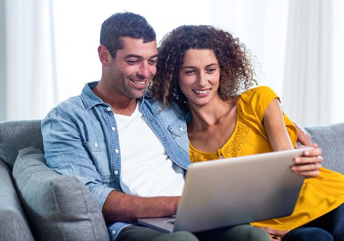 Casal abraçados enquanto estão sentados no sofá olhando para o laptop para identificar um birô de crédito