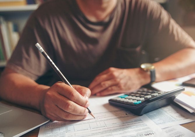 Mercado Pago: homem sentado em mesa de escritório com contas, calculadora e lápis da mão quitando suas dívidas com o Desenrola Brasil.