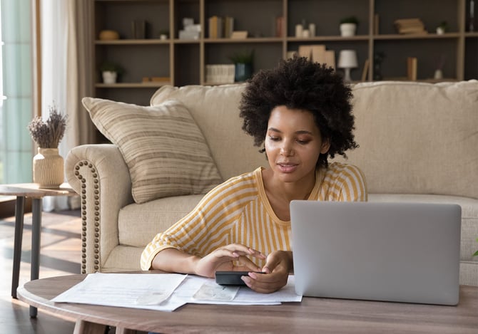 Mulher sentada na sala com notebook fazendo contas na calculadora para contratar um empréstimo com FGTS