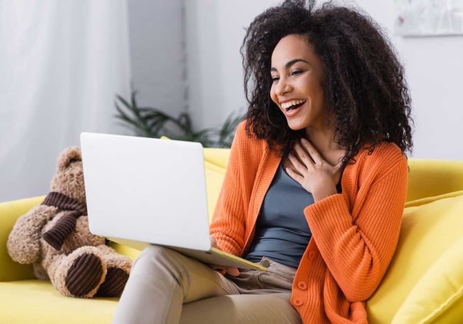 Mulher sentada e sorrindo para a tela do laptop que está em seu colo, enquanto verifica a contratação de um empréstimo consignado