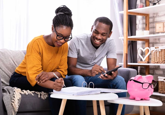 Casal sorrindo e sentado no sofá enquanto organizam suas finanças