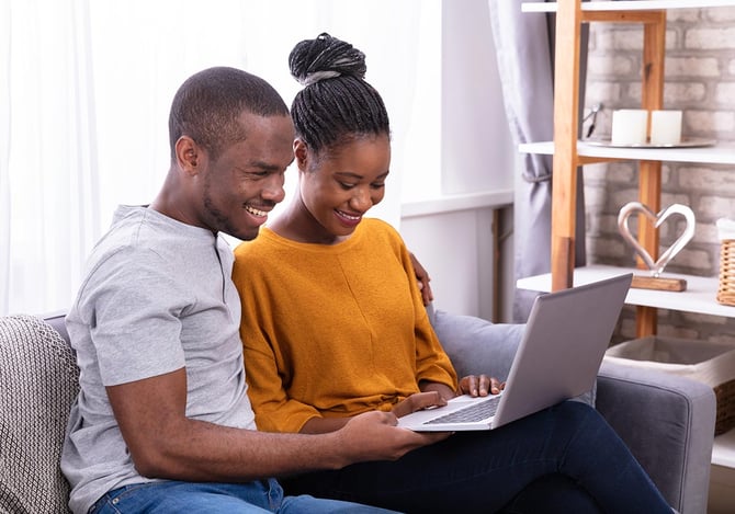 Casal sorrindo e sentados no sofá enquanto mexem no laptop