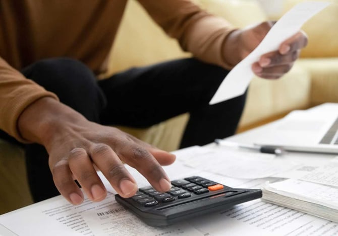 Um homem fazendo contas em uma calculadora, enquanto folheia alguns papéis