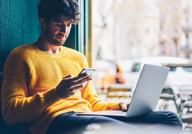 Homem mexendo no smartphone e no laptop