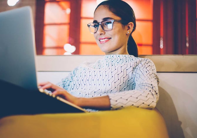 Mulher sorridente de óculos sentada no sofá com um notebook