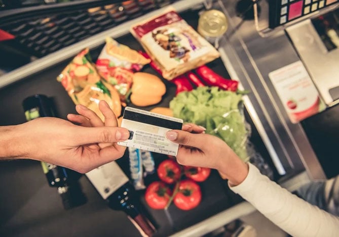 Duas pessoas segurando cartão de crédito com compras ao fundo