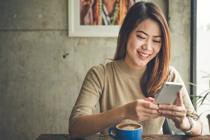 Uma mulher sorrindo enquanto olha para a tela de um celular. 