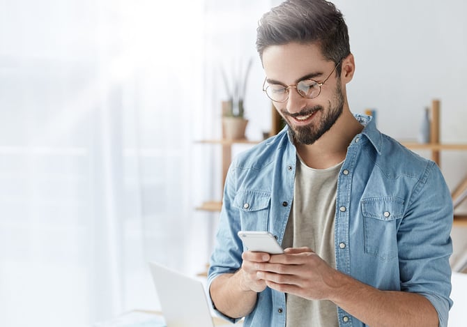 Homem de óculos sorrindo enquanto mexe no smartphone para investir em CDB pelo app Mercado Pago