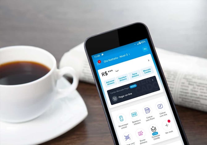 Um celular com a tela inicial do app Mercado Pago e ao fundo uma xícara de café