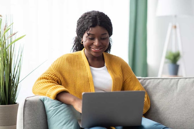 Uma mulher sorrindo enquanto olha para a tela de um notebook. 