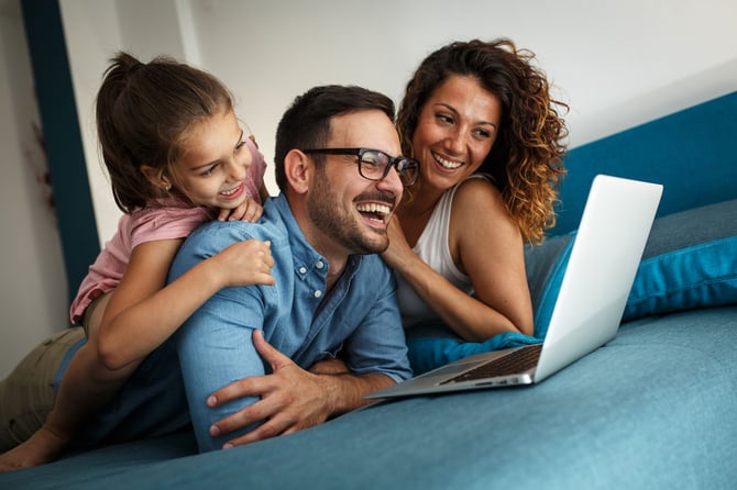 Um casal e uma criança deitados em uma cama, olhando para tela de um notebook