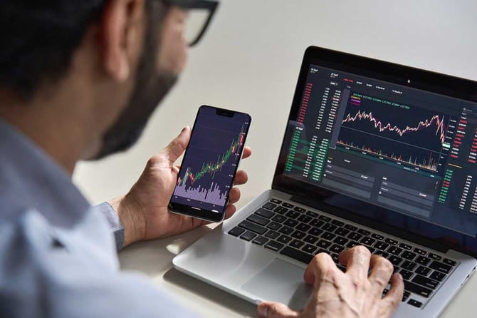 Um homem mexendo em um celular e um notebook que estão mostrando um gráfico.