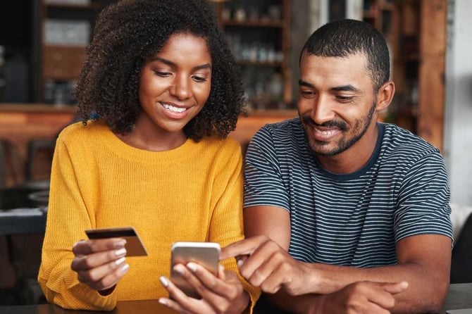 Um casal sorrindo, enquanto olha para a tela de um celular