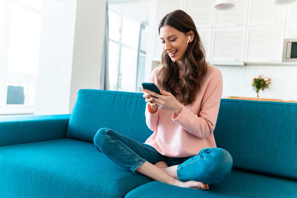 Mulher sentada em um sofá com um celular na mão e sorrindo