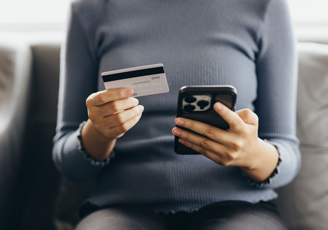 Mulher segurando cartão mercado pago enquanto faz uma transação segura no seu smartphone para evitar que caia no golpe do cartão clonado