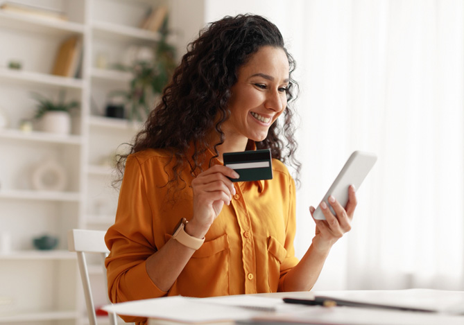 Mulher sorrindo enquanto segura seu celular e cartão de crédito Mercado Pago para recarregar seu celular através do app