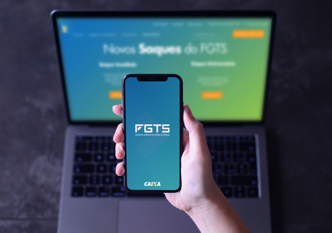Mercado Pago: imagem de um uma mão segurando um celular com o logo do aplicativo FGTS e um notebook aberto ao fundo em que o site do FGTS também está aberto, indicando o interesse de um cidadão em cancelar a modalidade de saque-aniversário.
