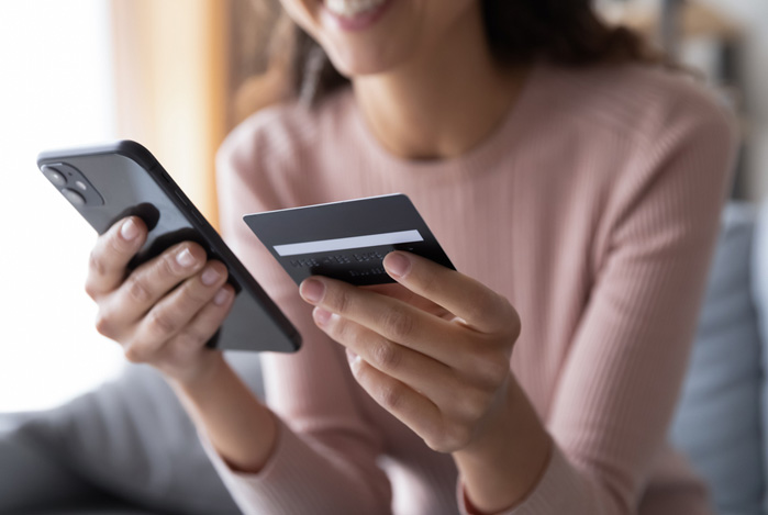 Mercado Pago: mulher segurando o celular e o cartão de crédito para realizar uma compra parcelada.