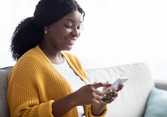 Mulher sorrindo enquanto utiliza um smartphone, demonstrando praticidade e facilidade de gerenciamento financeiro com uma conta digital.