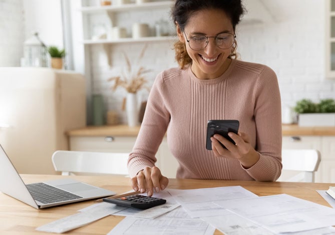 Mercado Pago: Mulher sorridente analisando documentos financeiros com celular e calculadora em mãos, representando a busca por alternativas para evitar dinheiro parado.