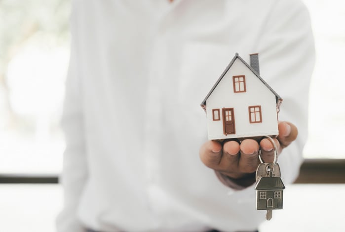 Mercado Pago: homem segurando um chaveiro em formato de casa com uma chave representando a aprovação no empréstimo imobiliário. 