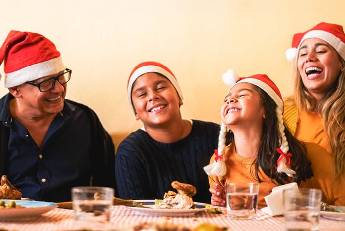 Mercado Pago: família reunida à mesa, todos sorrindo com chapéu de Papai Noel para celebrar a festa de Natal.