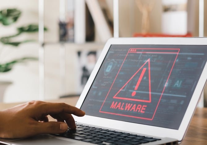 Mercado Pago: mão de uma pessoa mexendo no laptop aberto em cima de uma mesa de madeira e com a tela focada em uma alerta de Malware