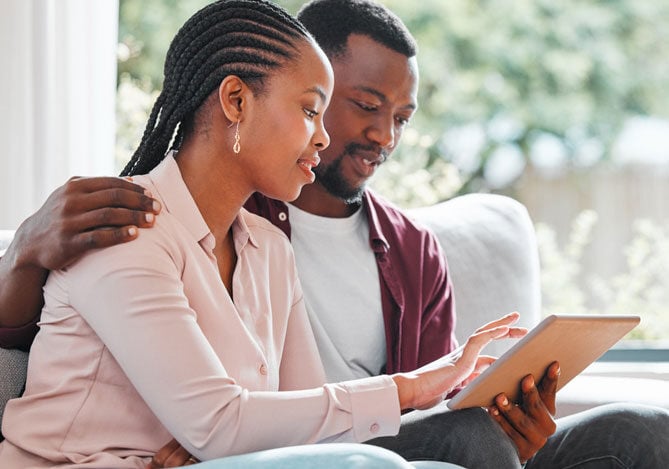 Mercado Pago: imagem de um casal sentado no sofá de casa. Ambos seguram um tablet no qual verificam o que é sinistro para entender melhor quais as informações que devem se atentar ao contratar um seguro residencial e um seguro veicular.