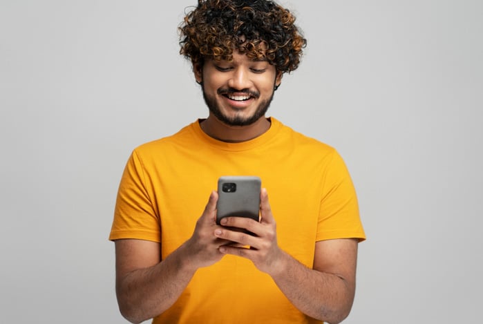 Mercado Pago: homem de camiseta amarela, olhando para o celular na sua mão, enquanto ele está sorrindo ao descobrir o que é crédito pessoal.