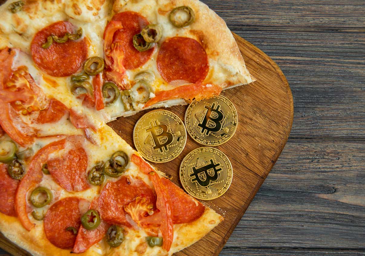 Pizza em uma tábua de madeira junto com moedas de Bitcoin